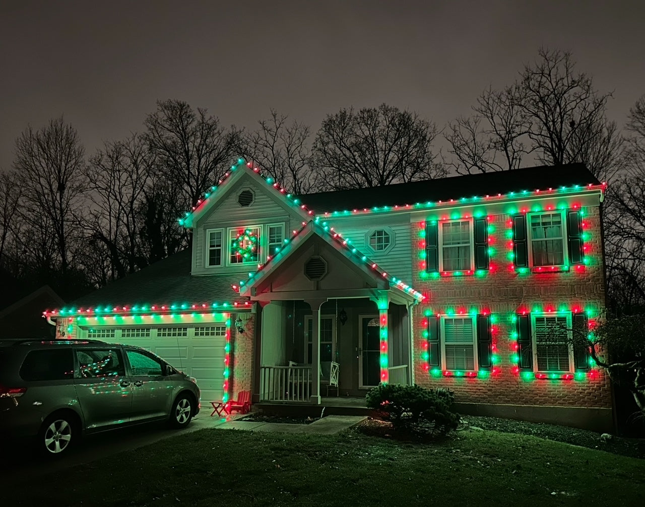 House decorated with red and green Christmas lights at night.